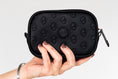 Load image into Gallery viewer, Hand holding the black ettellon leather Ryan pouch, featuring its embossed pattern and compact rectangular shape.