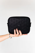Load image into Gallery viewer, Hand holding the black ettellon leather Jillian pouch, featuring its embossed pattern and compact rectangular shape.
