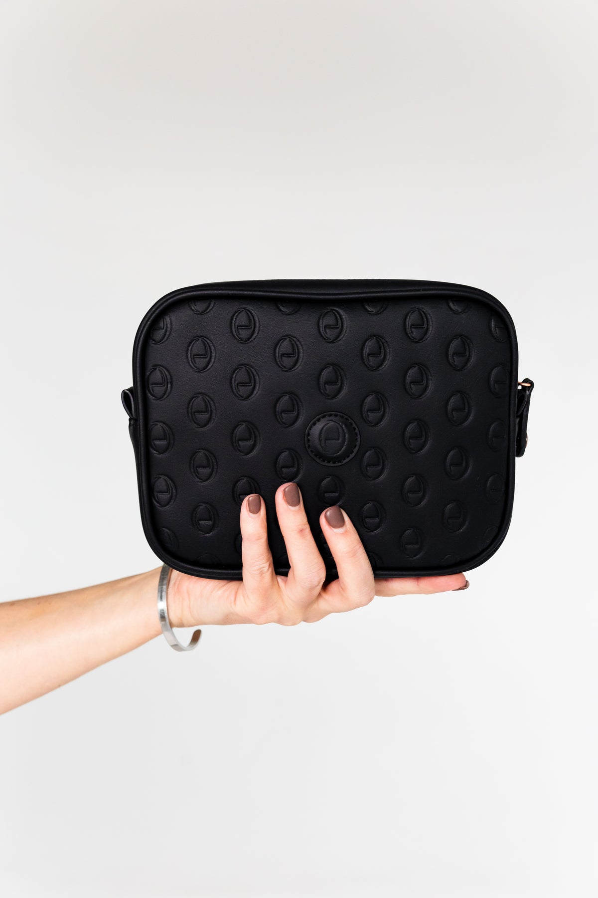 Hand holding the black ettellon leather Jillian pouch, featuring its embossed pattern and compact rectangular shape.