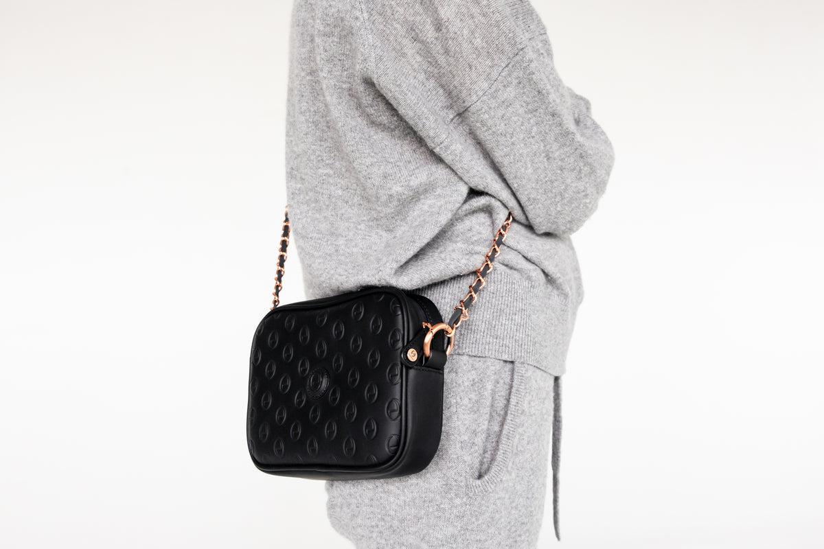 Woman wearing the black ettellon leather Jillian pouch as a crossbody bag with its removable chain strap.